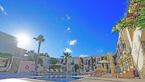 A pool area with sun loungers and umbrellas, surrounded by buildings with balconies and plants. - Ömer Aybak Beach Hotel (Bodrum)