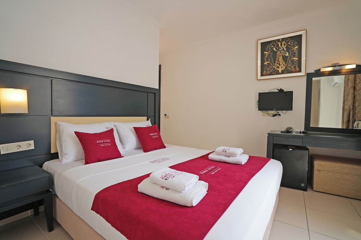 A hotel room with a neatly made bed, a bedside table, a desk with a mirror, and a television.