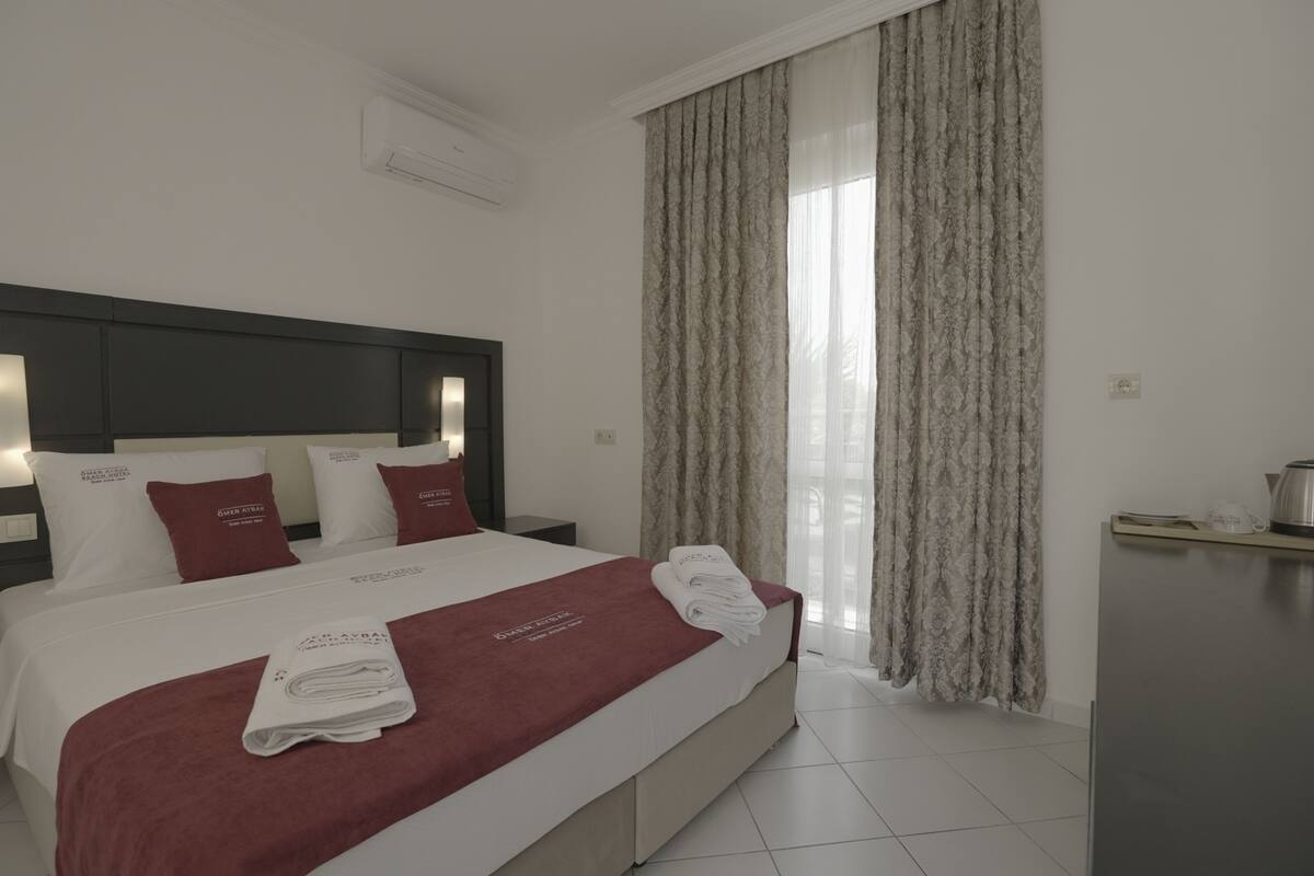 A hotel room with a large bed, a headboard, a bedside table, a wardrobe, and a window with curtains.