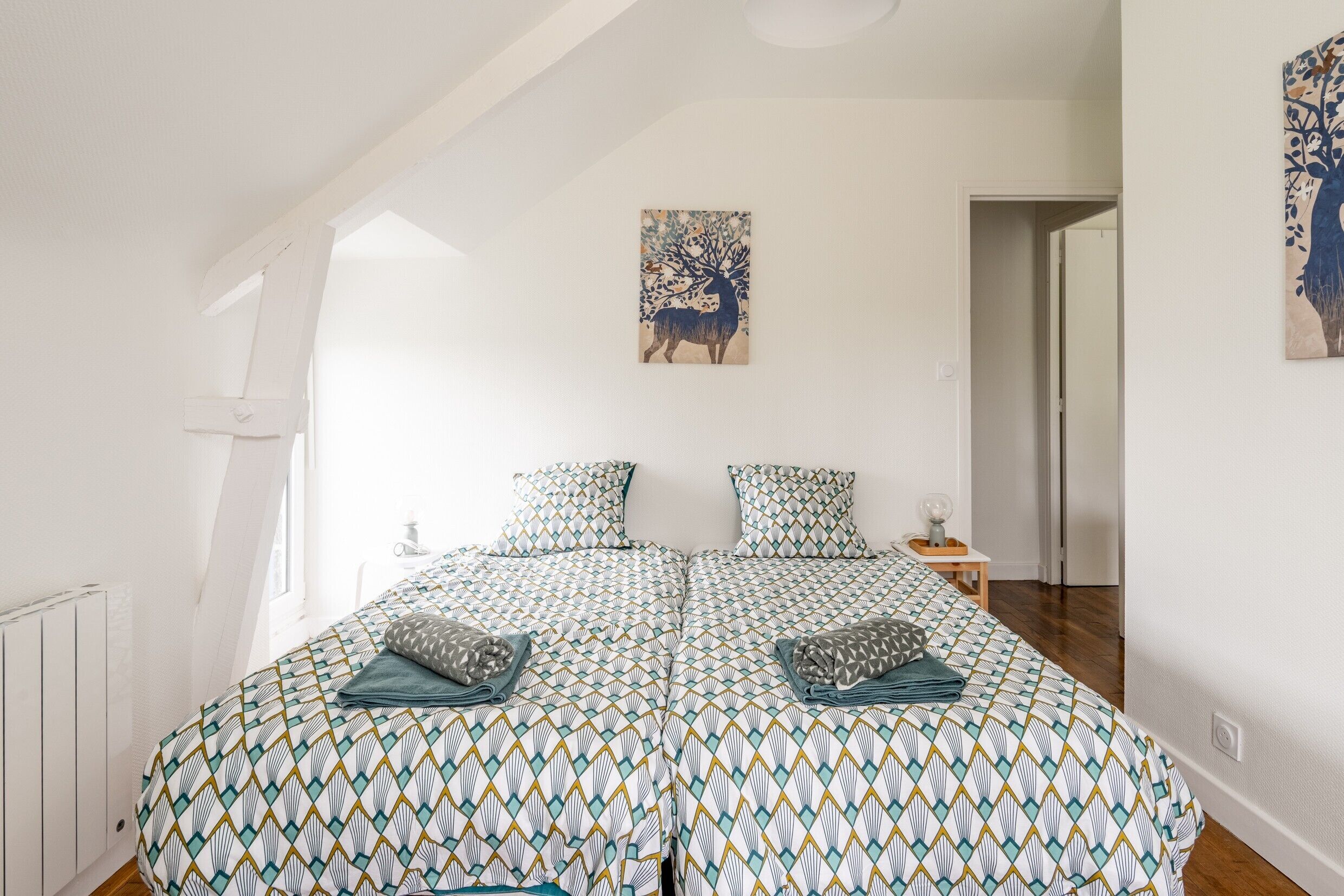 Ein Schlafzimmer mit einem gemusterten Bettbezug, einem Gemälde an der Wand und Blick auf den Flur.