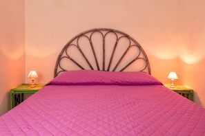 Ein Bett mit Kopfteil, zwei Nachttische mit Lampen und eine pinke gesteppte Bettdecke.