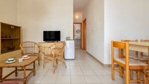 Une pièce comprenant une table et des chaises, un téléviseur, un lave-linge et une étagère où sont rangés de la vaisselle.