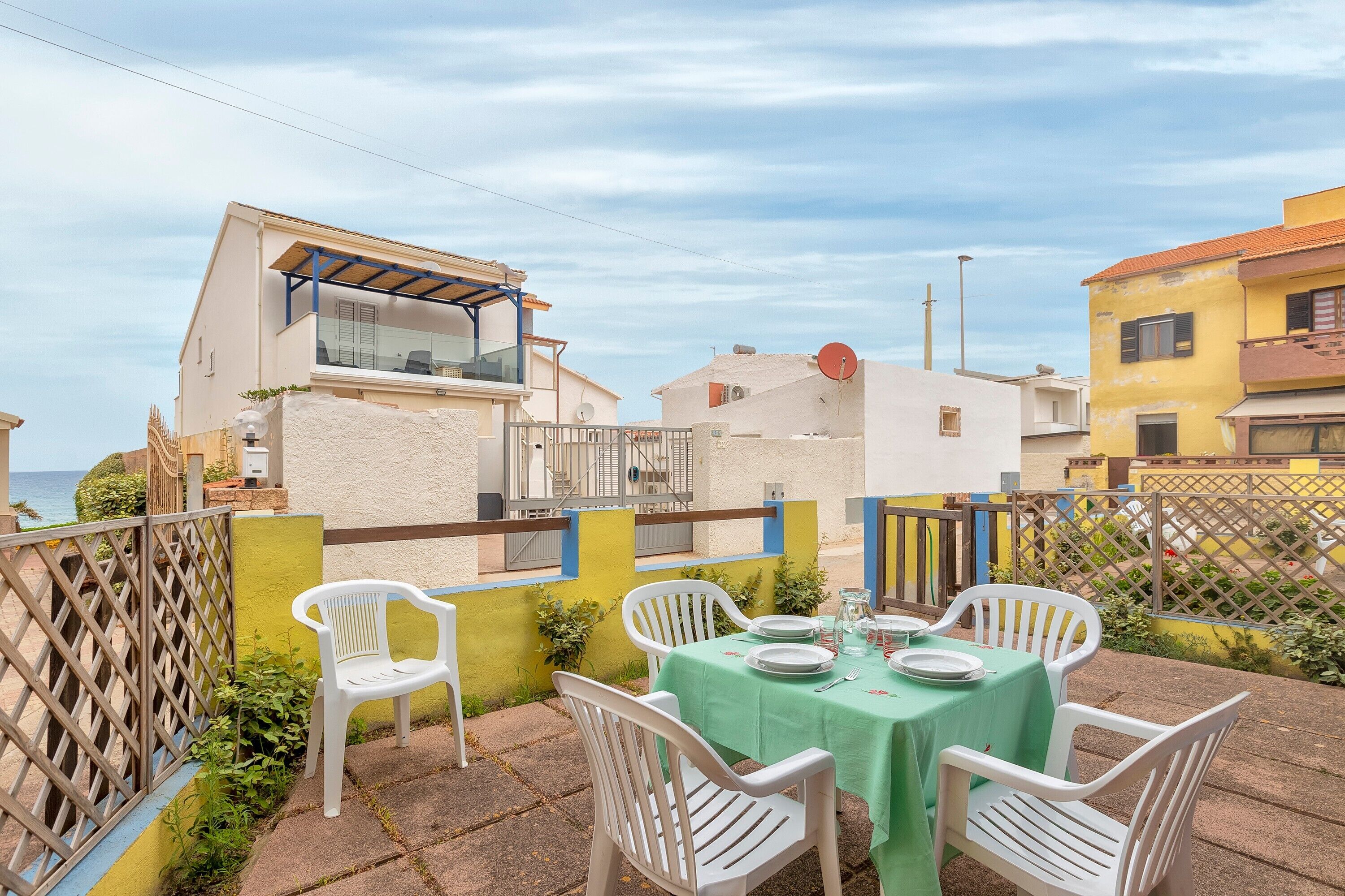 A patio with a table set for dining, white plastic chairs, and a green tablecloth.
