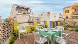 Une terrasse avec une table dressée pour le repas, des chaises en plastique blanches et une nappe verte.