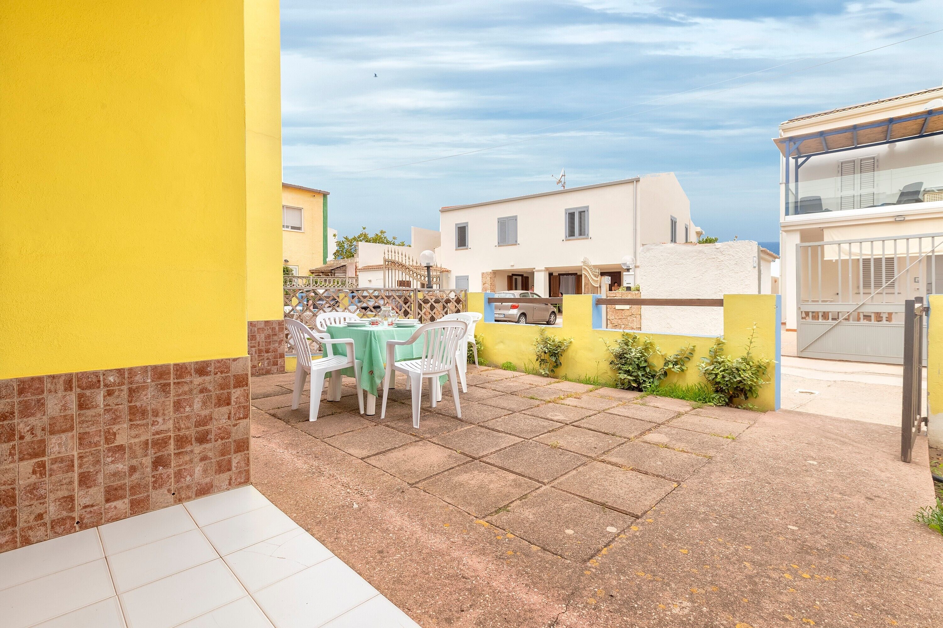 Une terrasse avec une table et des chaises, un sol carrelé et un mur jaune.