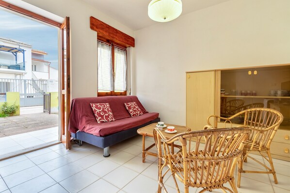 Ein Zimmer mit einer Couch, einem Esstisch mit Stühlen, einem Schrank und Blick ins Freie.