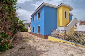 A two-story house with a blue and yellow facade, a staircase, and a garden with flowering plants.