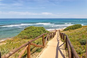 Ein Küstenweg, der zum Strand führt, mit Holzgeländern und viel Grün.