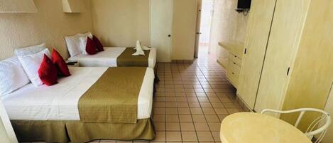 Habitación de hotel con dos camas, una mesita, una silla, un armario y un ventilador de techo.