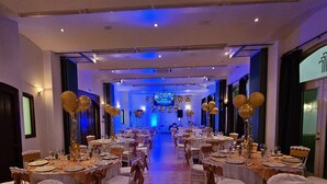 A banquet hall with tables set for a formal event, featuring gold balloons and a stage in the background. - HOTEL HACIENDA DEL RIO (Yautepec)