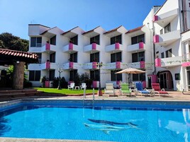 Un hotel con piscina, mobiliario exterior y balcones con plantas en macetas.