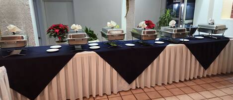 Una mesa de buffet con varias estaciones de servicio, manteles blancos y un suelo de baldosas.