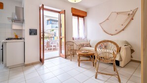 Una habitación con mesa de comedor, sillas, sofá, zona de cocina y balcón.
