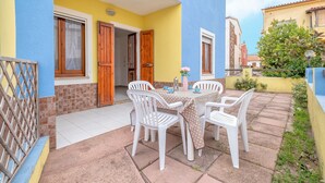 Un patio con una mesa, sillas, una puerta de madera y una pared amarilla.