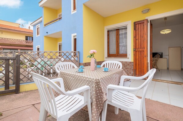 A patio with a table and chairs, a wooden door, and a window with a curtain. - Apartment 'Brezza Marina 6' with Private Garden and Air Conditioning (Lu Bagnu)