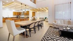 A modern kitchen with wooden cabinets, a dining area with a long table and chairs, and a living room with a sofa and coffee table. - Hermosa villa rodeada de montañas, Combina elegancia moderna con la naturaleza. (Bonao)