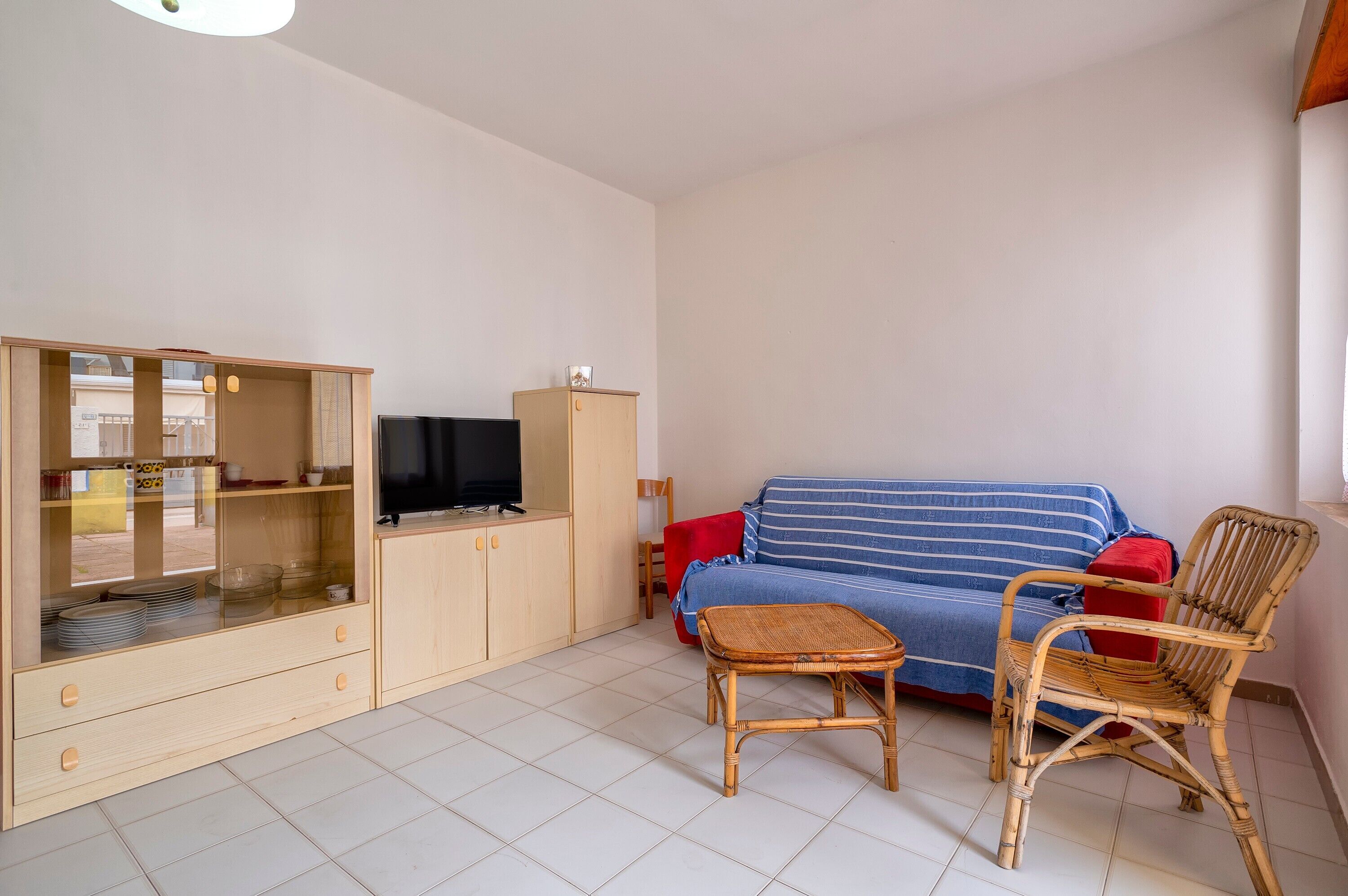 Ein Wohnzimmer mit einer Couch, einem Fernseher, einem Schrank und einem Korbstuhl.
