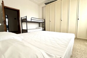 A single bed with a white mattress and a bunk bed to the left. There is a wardrobe with multiple doors and a door leading to another room. - SE091 - Senigallia, three-room apartment with balcony near the sea (Senigallia)