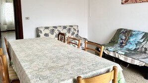 Una habitación con una mesa de comedor, sillas de madera, un sofá con funda estampada y una pared decorada con una pintura de un paisaje urbano.