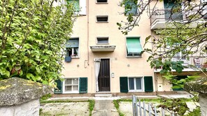 Un edificio con entrada central, varias ventanas con contraventanas y un pequeño jardín.