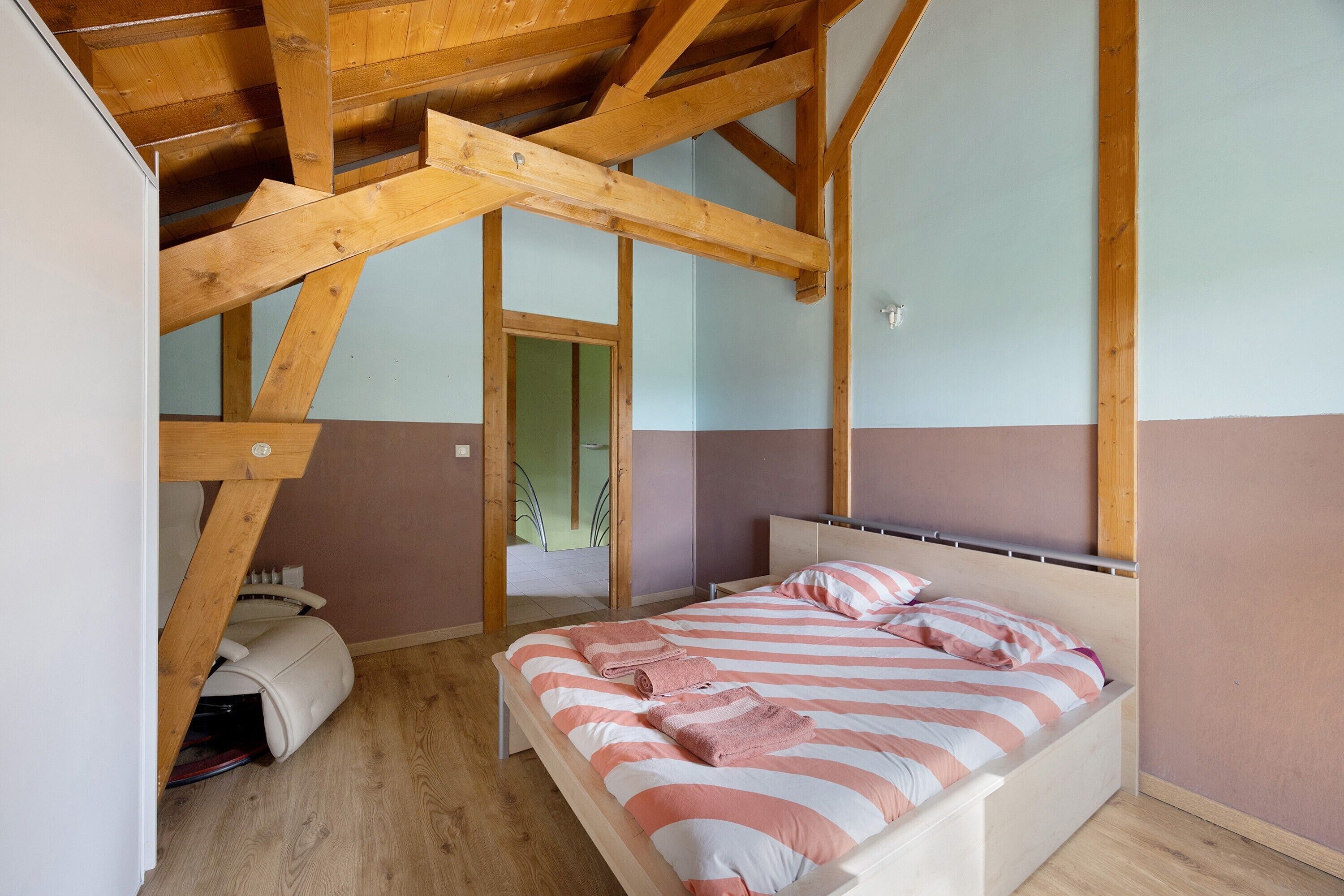 Une chambre avec un plafond en bois, un lit avec une literie à rayures et une porte visible qui mène à une autre pièce.