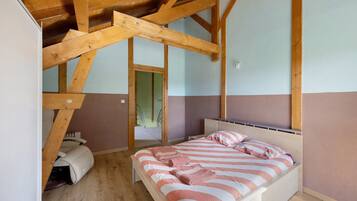 Une chambre avec un plafond en bois, un lit avec une literie à rayures et une porte visible qui mène à une autre pièce.