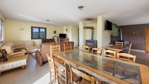 A living room with a sofa, a glass-top dining table, and a television. - Cottage 'Villa De St Off' with Mountain View, Private Terrace and Wi-Fi (Saint-Offenge)