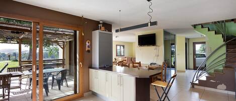 A modern kitchen with a dining area, a TV mounted on the wall, and a staircase leading to another level.