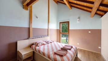 Un dormitorio con techo de madera, una cama con ropa de cama a rayas, una mesita de noche y una ventana.
