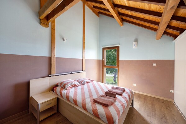 A bedroom with a wooden ceiling, a bed with striped bedding, a bedside table, and a window.