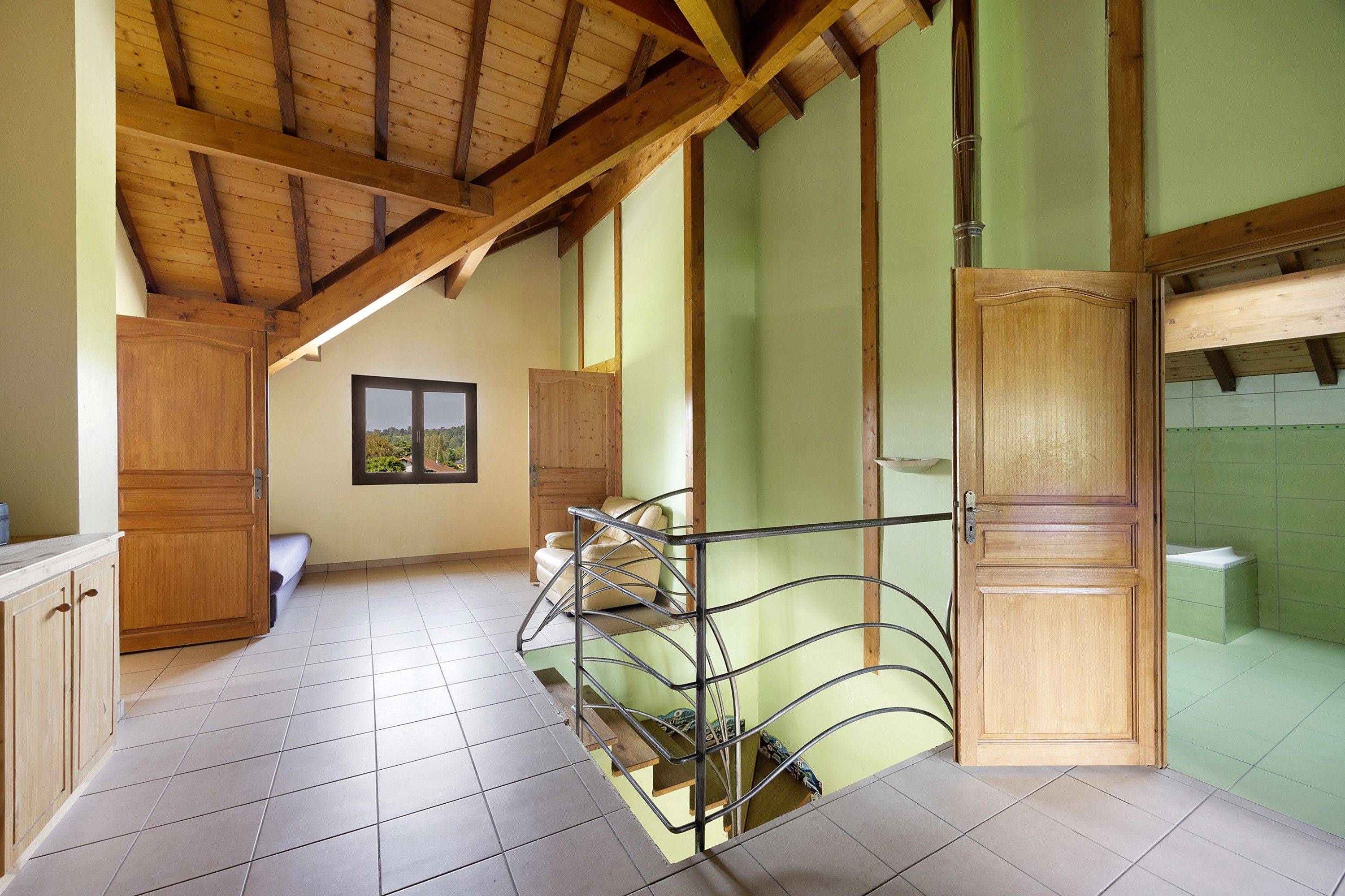 Una habitación con techo de madera, suelo de baldosas, puerta de madera, ventana con vistas y una silla de metal.