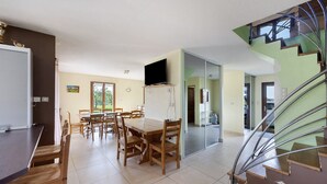 A spacious kitchen with a dining area, a TV mounted on the wall, and a staircase leading to an upper level. - Cottage 'Villa De St Off' with Mountain View, Private Terrace and Wi-Fi (Saint-Offenge)