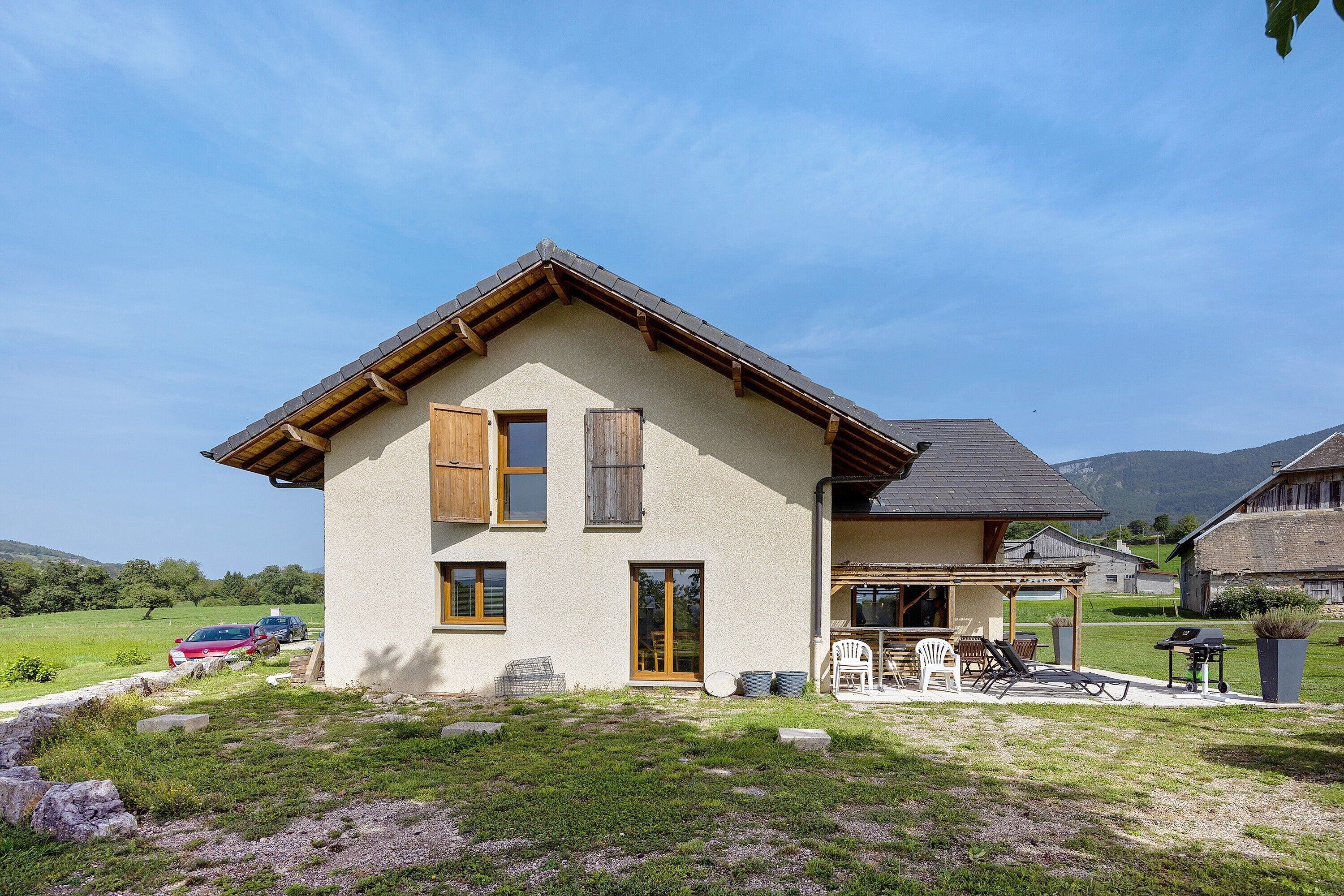 Une maison à deux étages avec un toit en pente, une véranda à l’avant dotée de sièges extérieurs et un garage visible.