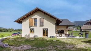 A two-story house with a sloped roof, a front porch with outdoor seating, and a visible garage. - Cottage 'Villa De St Off' with Mountain View, Private Terrace and Wi-Fi (Saint-Offenge)