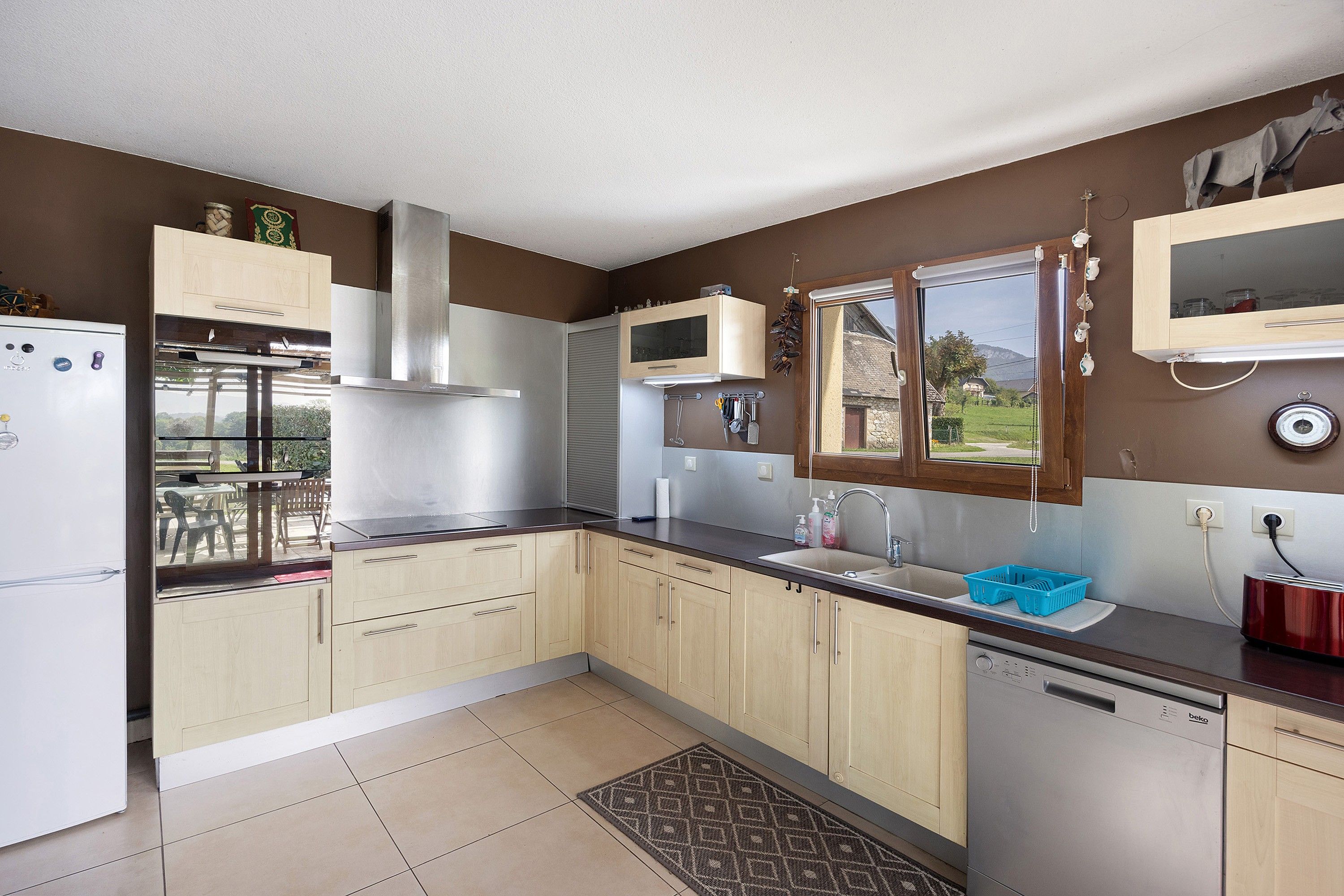 Una cocina moderna con horno integrado, lavavajillas y ventana con vistas a un jardín.