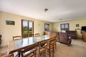 A dining area with a glass-top table and wooden chairs, a sofa, and a television.