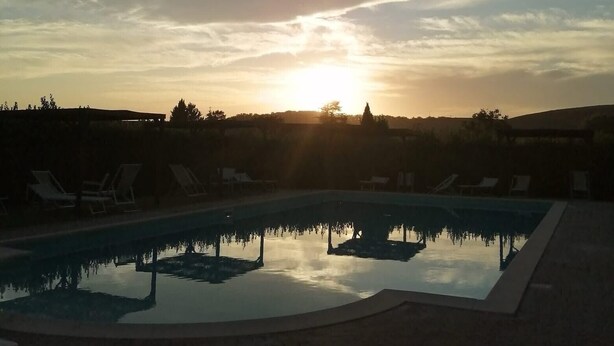 Una piscina con sillones de descanso, rodeada por un muro bajo, bajo un cielo al atardecer.