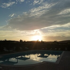 Una piscina con sillones de descanso, rodeada por un muro bajo, bajo un cielo al atardecer.