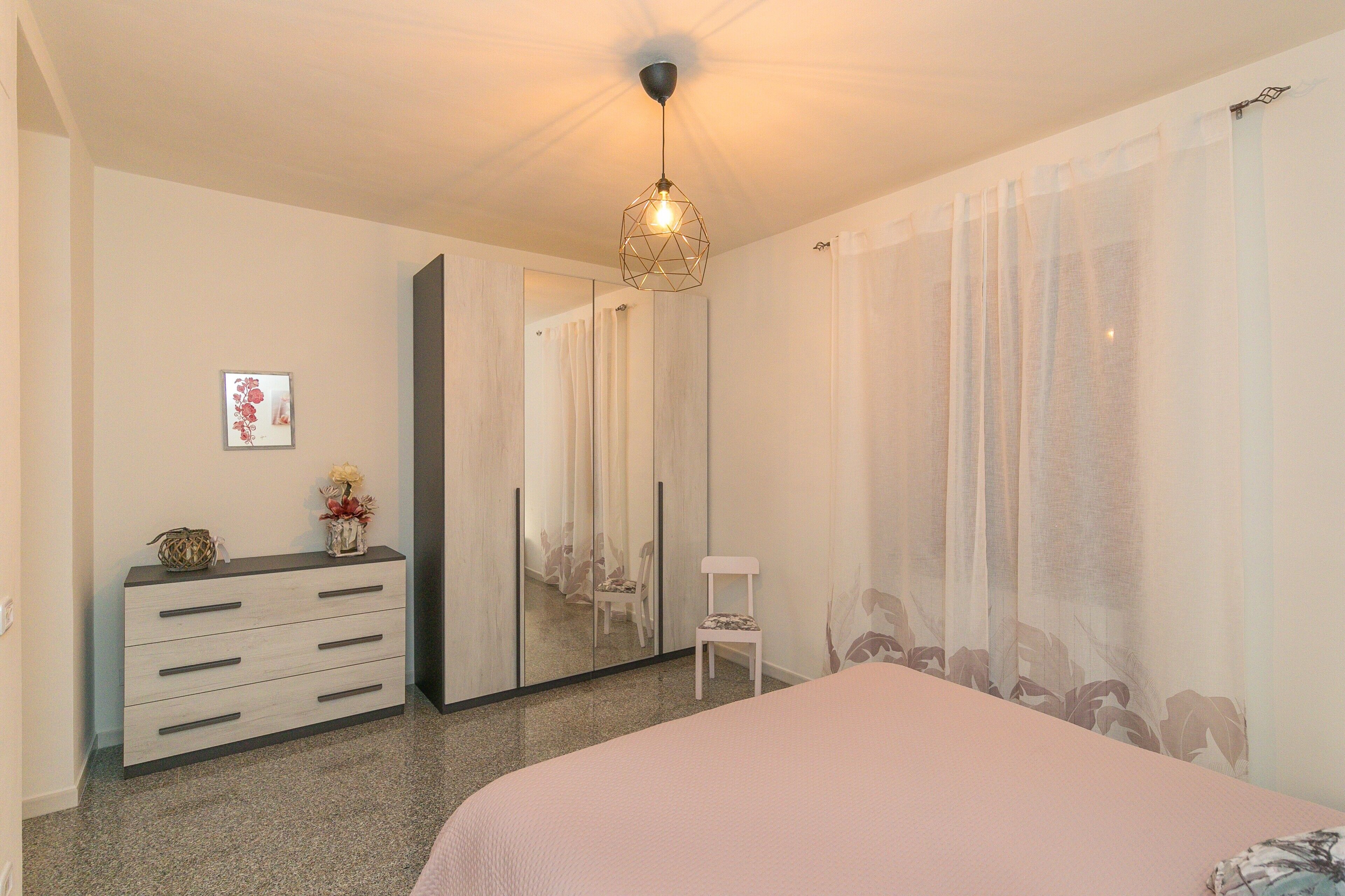 Une chambre à coucher avec un lit, une commode, une chaise, un miroir et un luminaire au plafond.