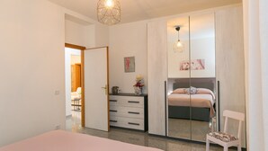 Un dormitorio con una cama, un aparador, una silla, un espejo y una lámpara colgante.