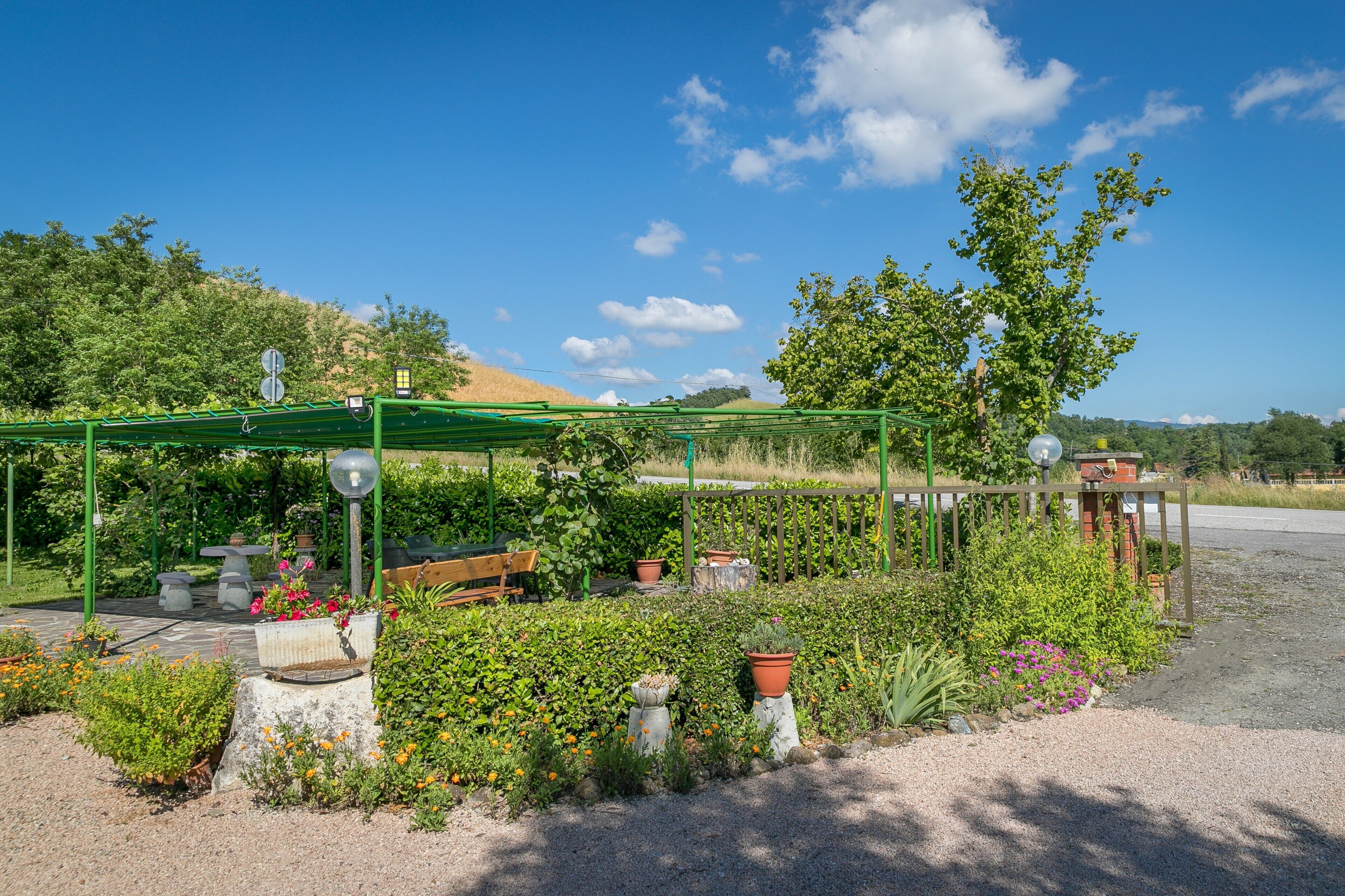 Jardí amb una pèrgola, bancs i plantes en testos.