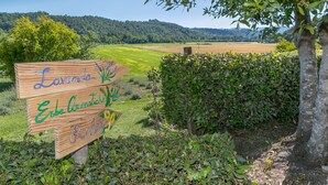 Un letrero de madera con la inscripción 'Lavanda Erbe Aromatische Relax', rodeado de follaje y con vistas a un campo.
