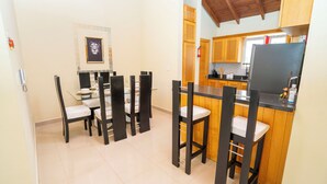 A compact kitchen with wooden cabinets, a black countertop, and a dining area with black chairs and a glass table.