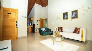 A modern living room with a white sofa, green armchair, and a glass coffee table. There is a wooden door labeled "3-B" and a kitchen area in the background.
