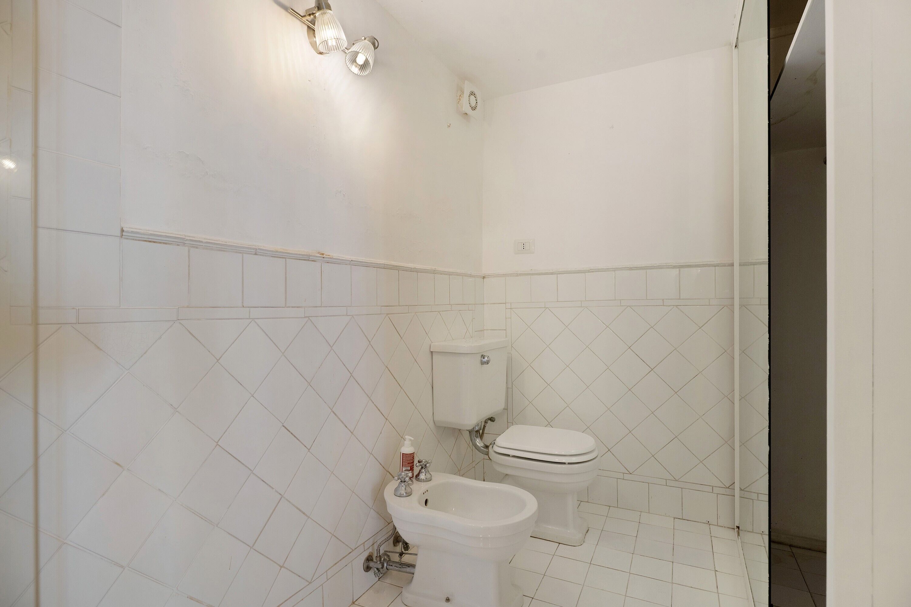 A bathroom with a toilet, bidet, and a wall-mounted light fixture.