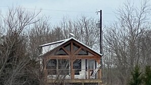 A wooden cabin with a balcony, situated by a body of water, surrounded by leafless trees.