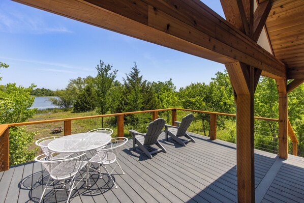 Une terrasse en bois avec une table et des chaises, donnant sur un lac et entourée d’arbres.