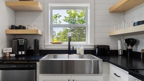 Una cocina moderna con un lavamanos de acero inoxidable, armarios blancos y estantes de madera.