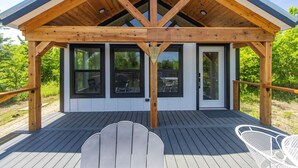 A wooden deck with a covered seating area, large windows, and a view of the surrounding greenery.