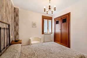 Un dormitorio con cama, una silla, un armario de madera, un radiador y una araña.